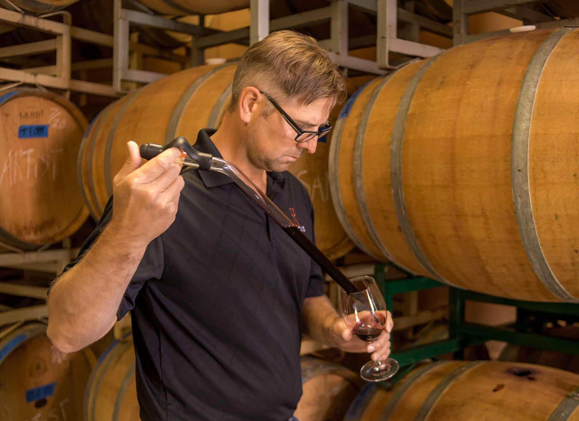 Ned Morris testing wine in front of barrels of wine.