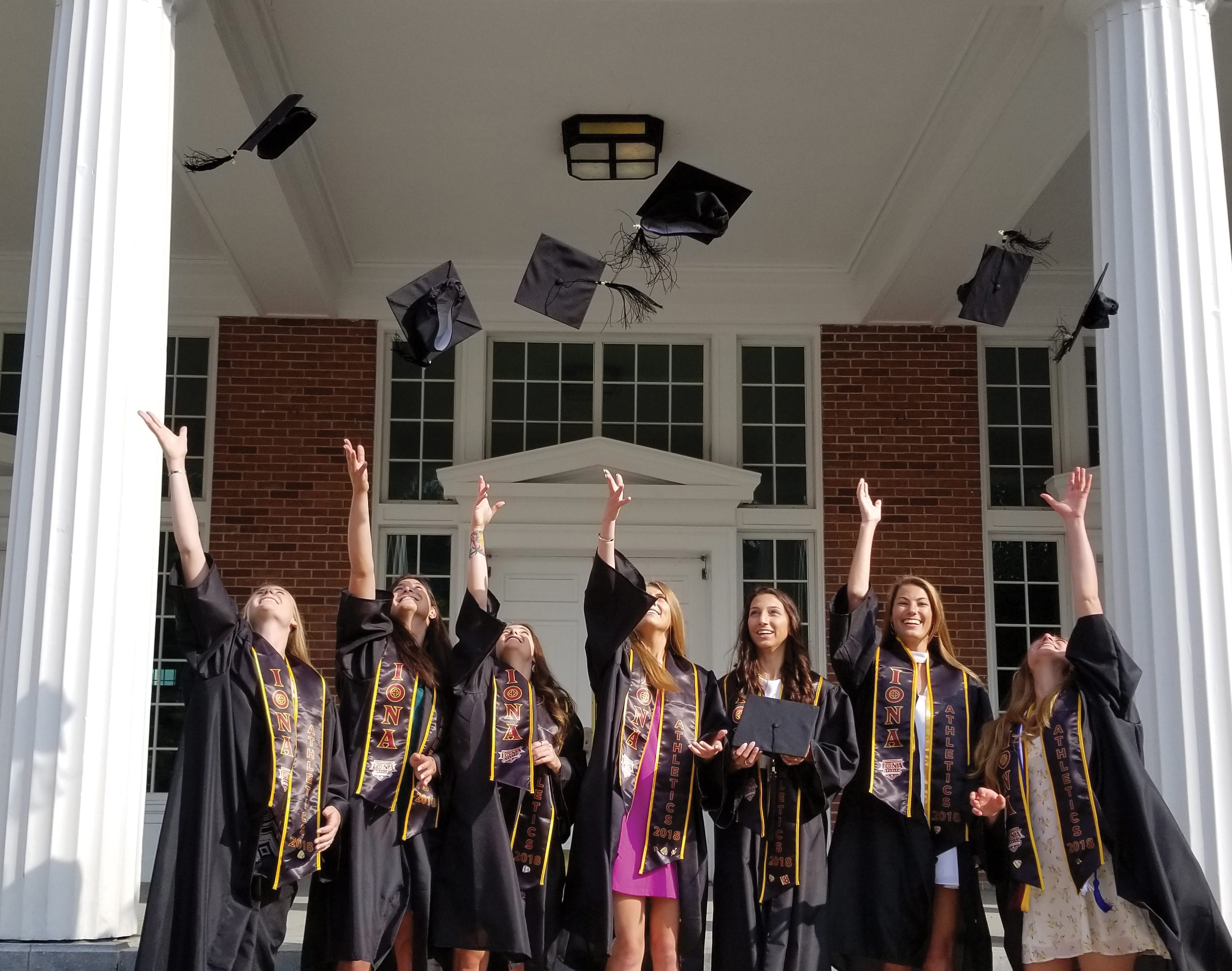 Seven students in front of Spellman hall throwing their graduation caps in the air.