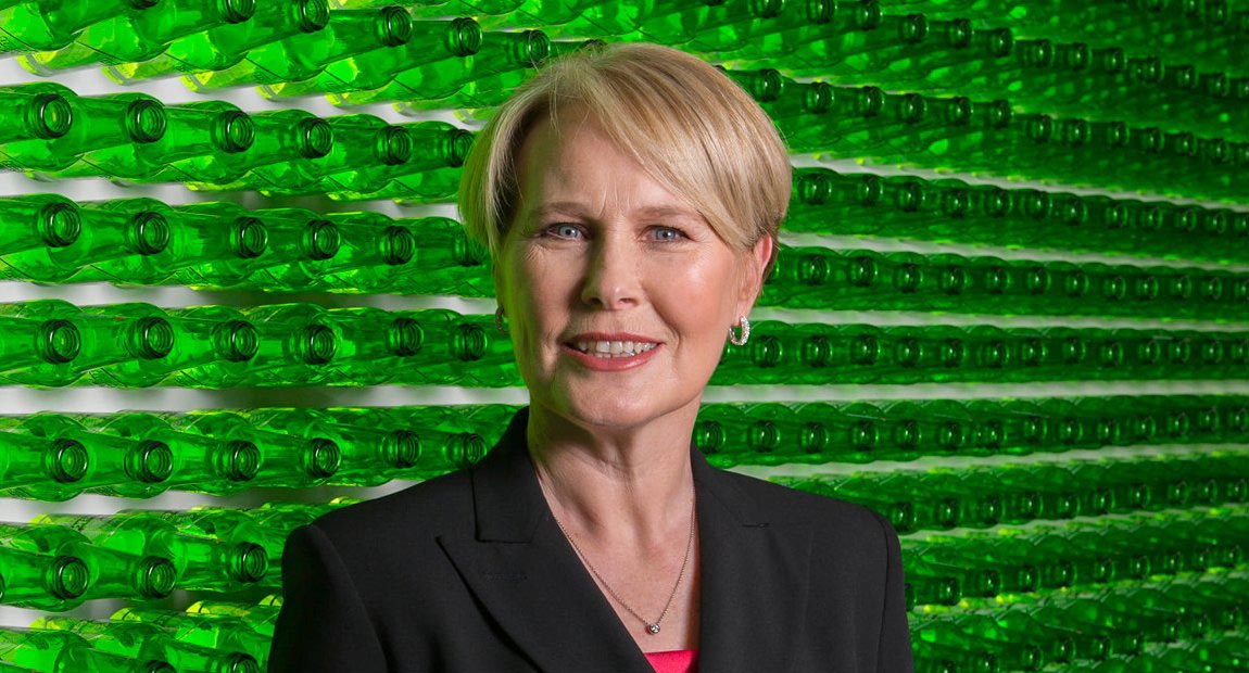 Margaret C Timoney in front of a wall of Heineken bottles.