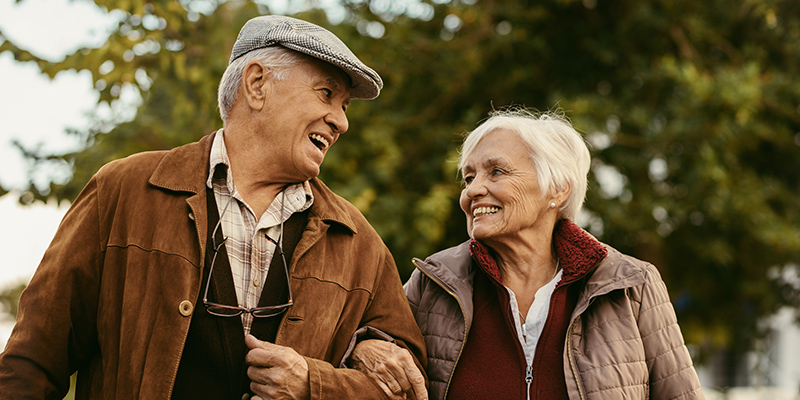 A Man and wife walk outdoors arm in arm.