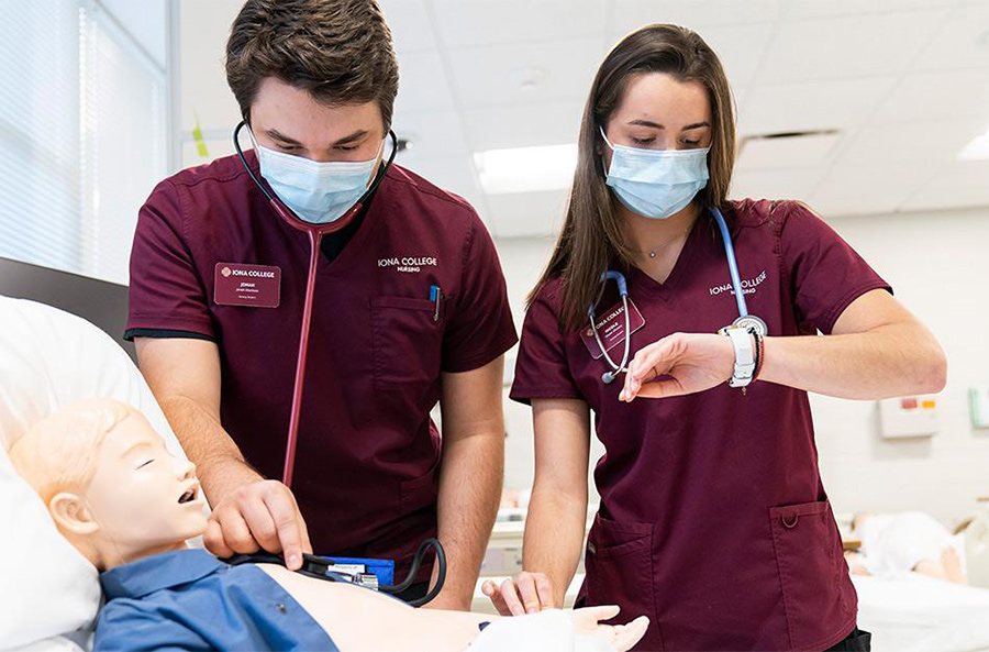 Two students work on a mannequin patient in the nursing lab.