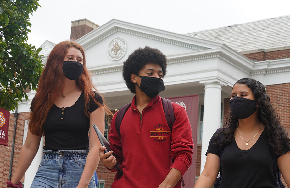 Three students with facemasks walk past McSpedon Hall.