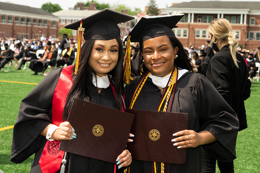 Two graduates in regalia hold their diplomas at the 2021 in-person recognition ceremony.