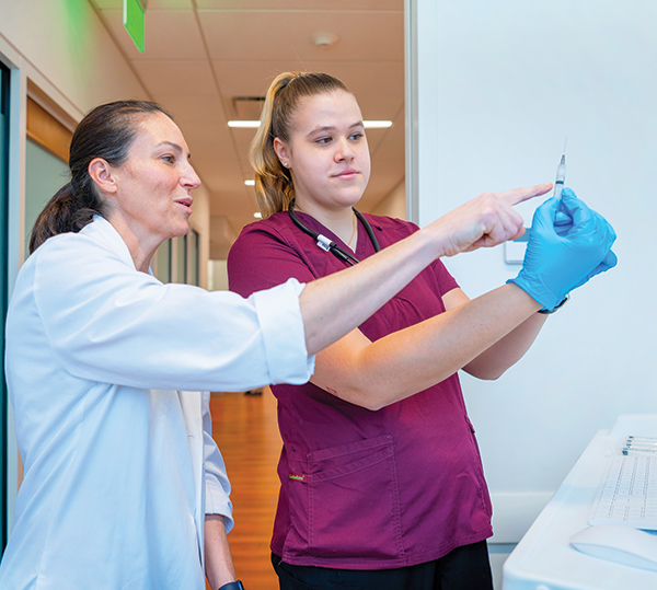 A nursing student and professor review how to handle a syringe.