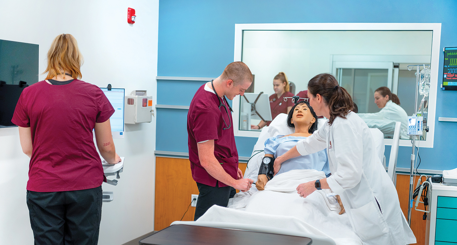Two nursing students and a professor practice on a mannequin.