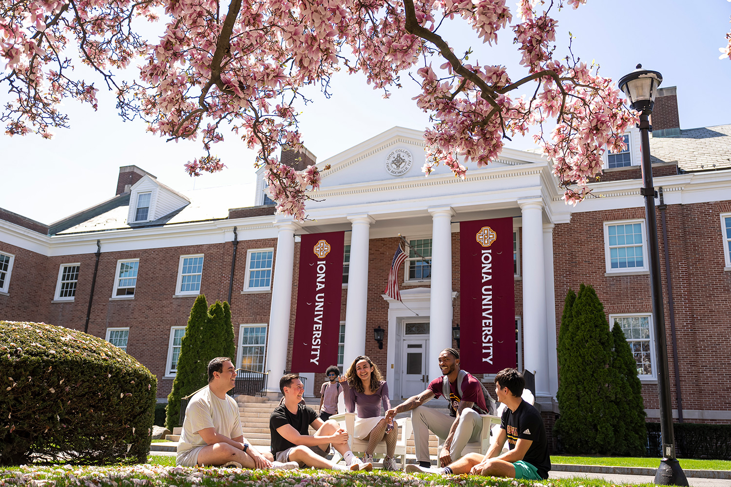 Iona students sit outside of McSpedon Hall on a sunny day and chat.