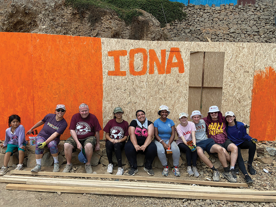 Iona mission leaders, students and residents of Jicamarca in front of a house under construction with Iona painted on it.