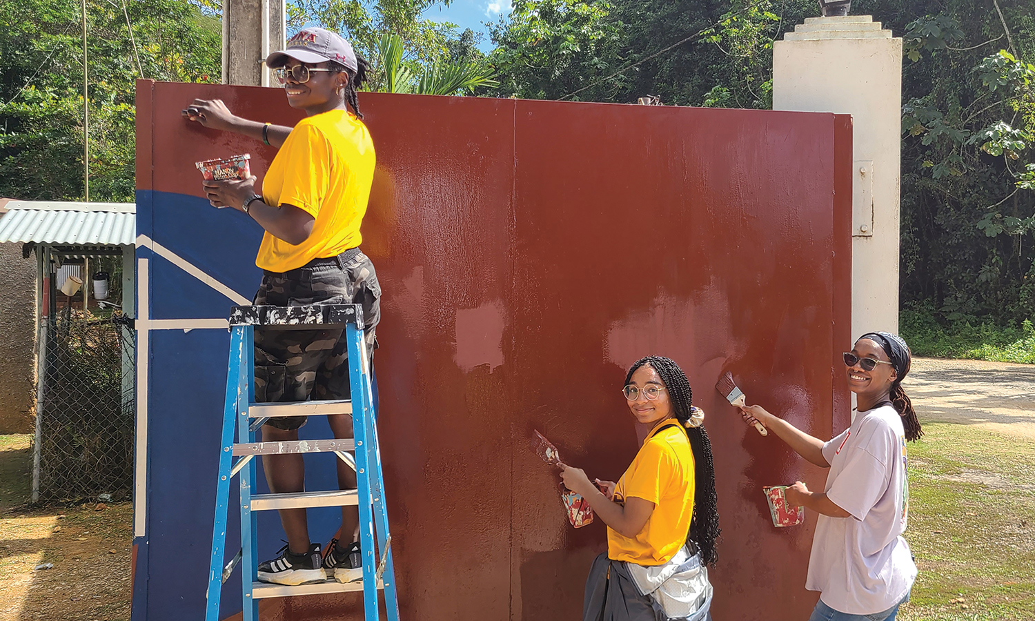 Two students and a mission trip leader paint a wall.